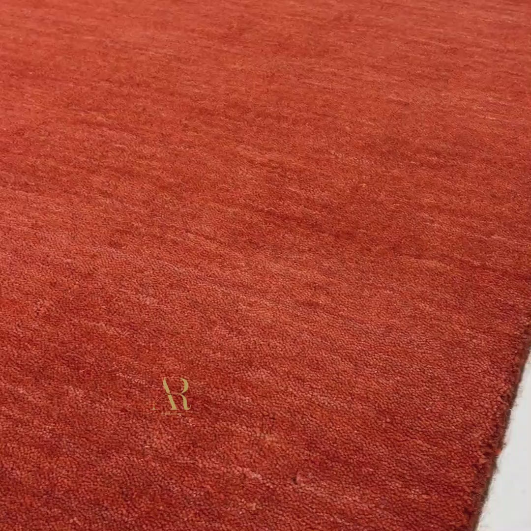 A rectangular area rug in a rich rust red color with a subtle textured pattern and a small gold butterfly motif in the upper left quadrant, shown against a plain white background.