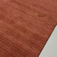A close-up of a rust-brown textured rug with a small gold embroidered letter 'AR' on a light-colored floor.